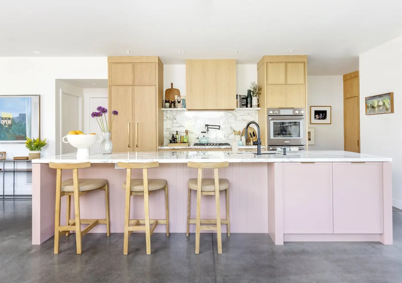 Finished kitchen with a blush-pink island, marble backsplash and wood stools