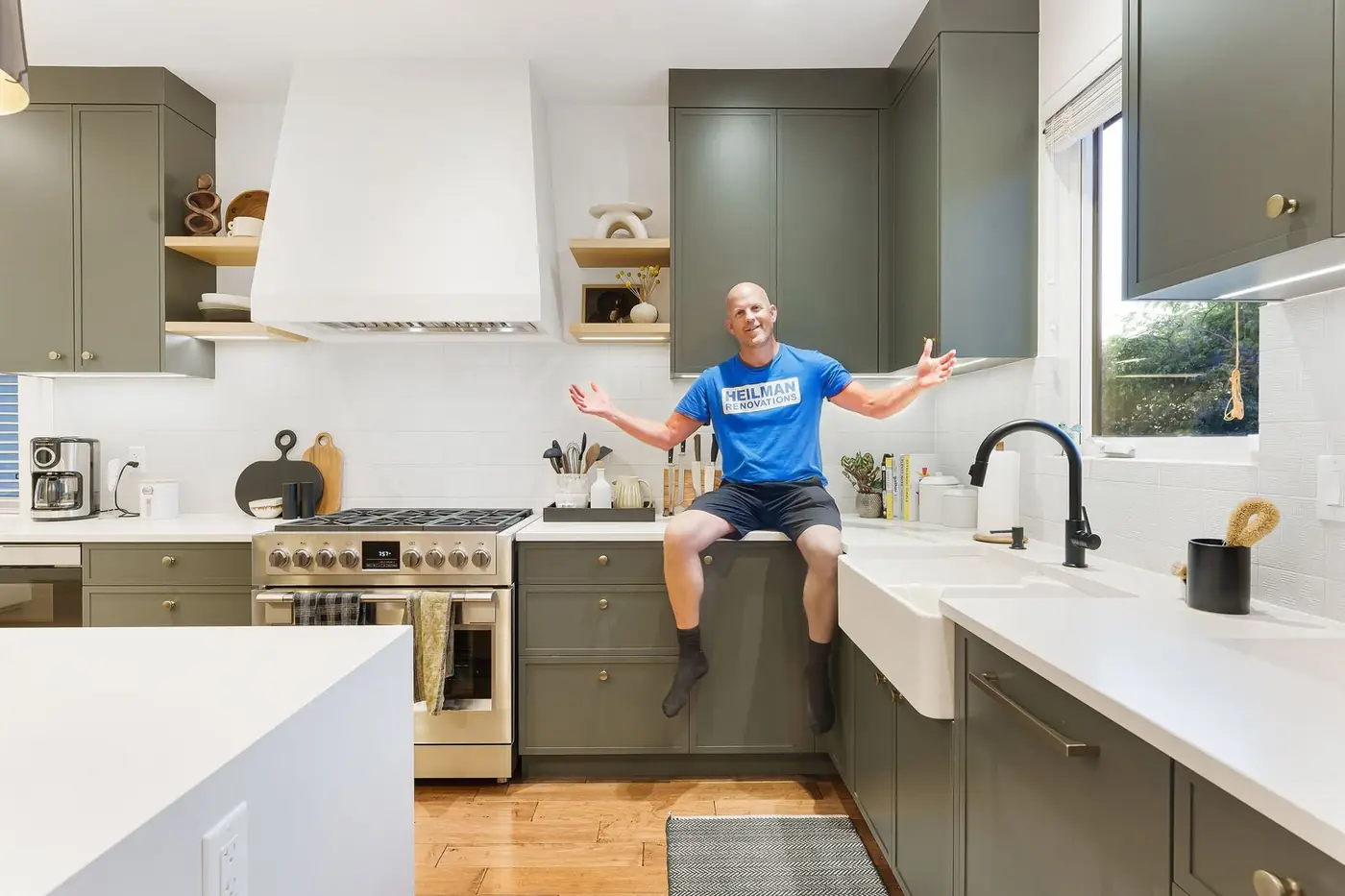 Joey Heilman sitting on the counter of a finished sage-green kitchen