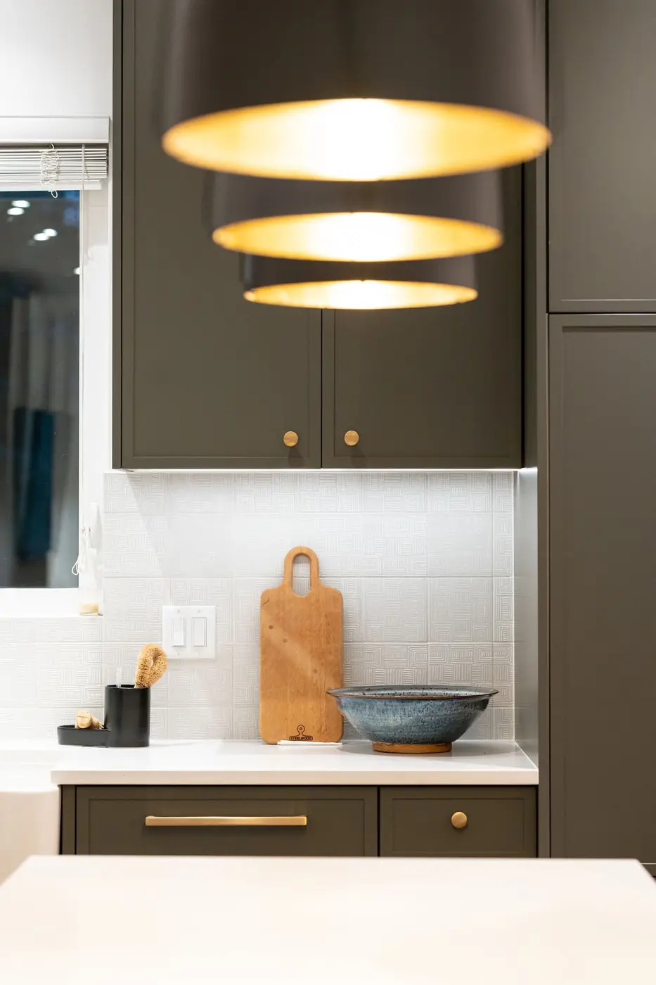 Brass pendant lights over a dark green kitchen wall