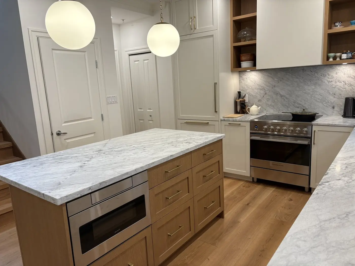 Finished kitchen with a marble-topped island, open shelving and globe pendants