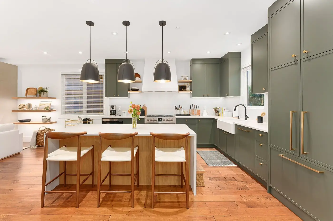 Sage-green kitchen with a waterfall island and three black pendants