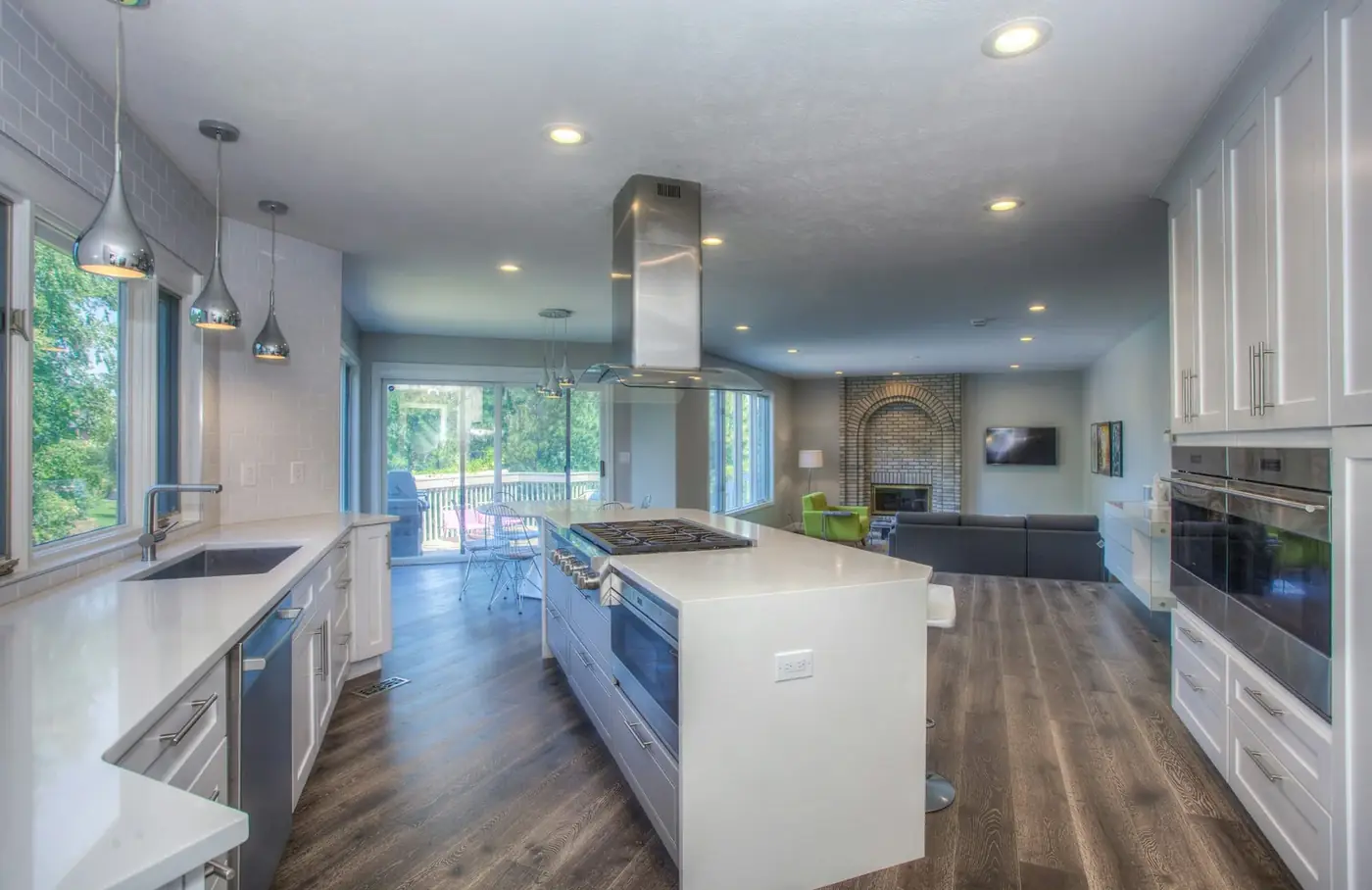 A white kitchen with a long island and steel pendant hood