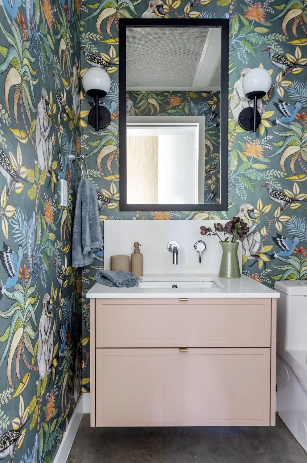 Powder room with botanical wallpaper, black mirror and a pale pink floating vanity