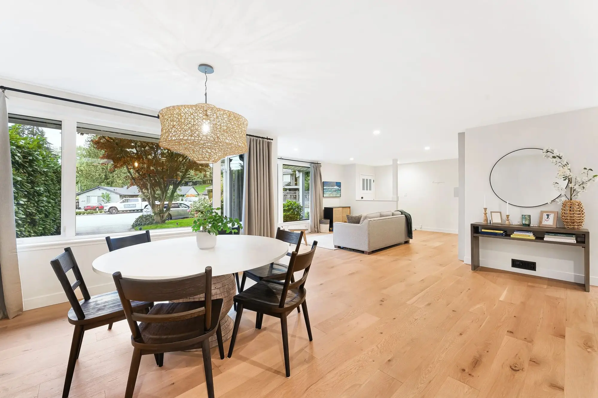 A renovated dining room with a round table, a woven pendant light and white-oak floors