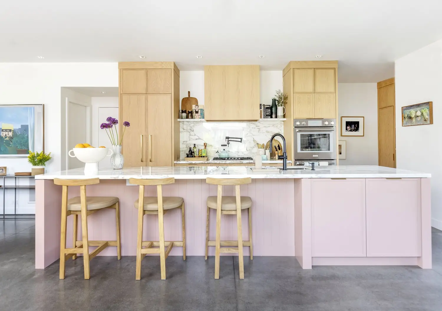 Finished kitchen with a blush-pink island, white counters and three wood stools