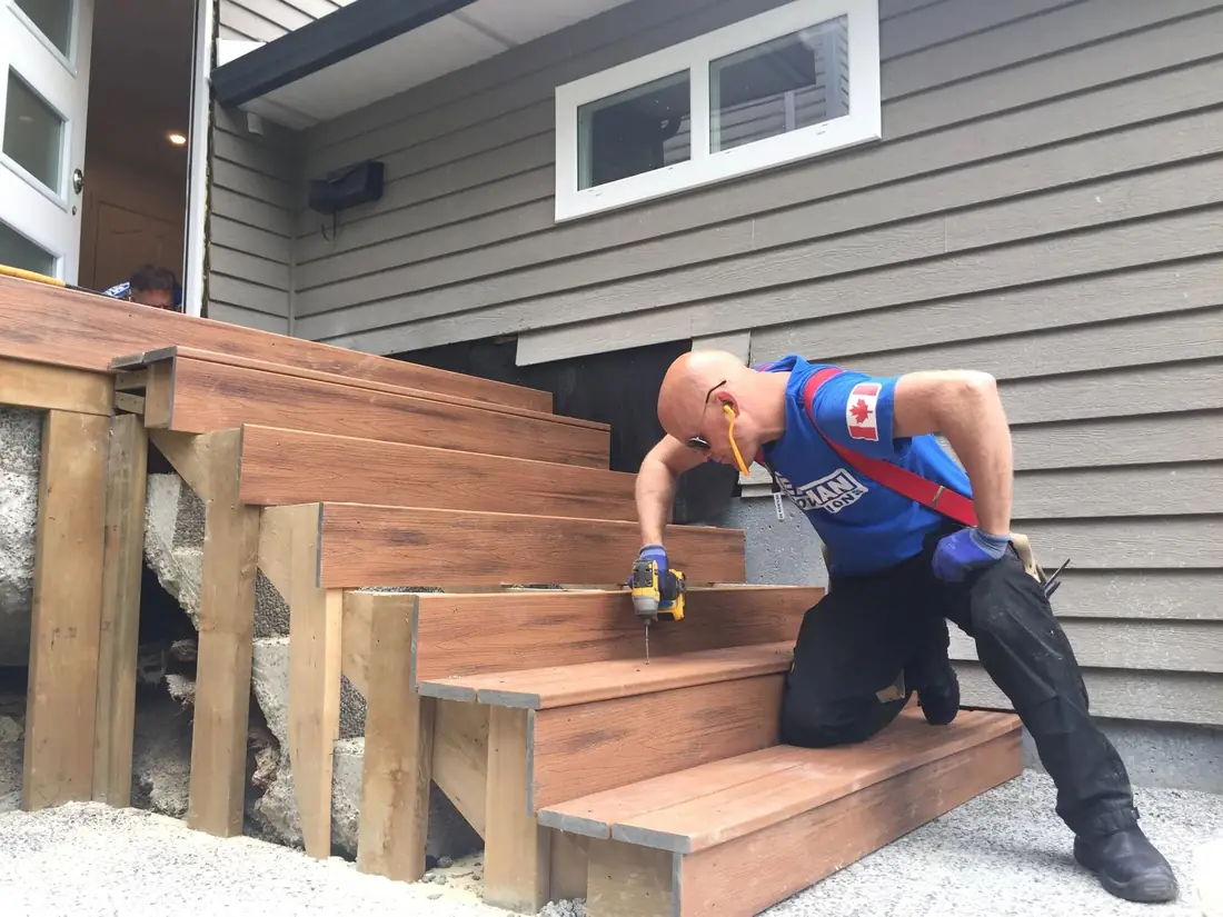 Crew member in a blue Heilman shirt building wooden deck stairs